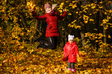 Mother and daughter having fun in the autumn park among the falling leaves.