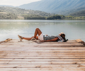 general view of a woman lying on a wooden dock of a lake. concept of rest and relaxation at sunset.