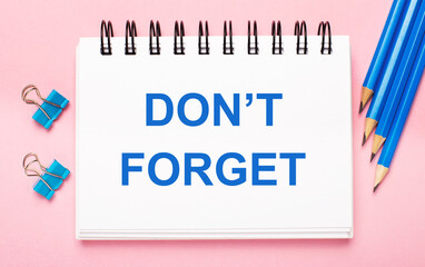 On a light pink background, light blue pencils, paper clips and a white notebook with the text DO NOT FORGET