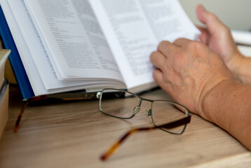 Naklejka premium A pair of glasses on a desk with a person reading a book.