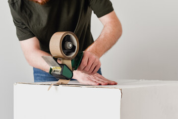 Detalle de un hombre usando una herramienta para precintar una caja de cartón con cinta adhesiva...