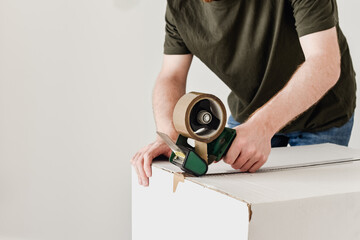 Fototapeta na wymiar Detalle de un hombre usando una herramienta para precintar una caja de cartón con cinta adhesiva marrón. Embalaje de cajas de mudanza.