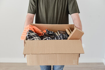 Un hombre joven sostiene una caja de mudanza, llena de ropa, libros y un marco de foto.
