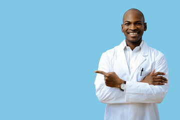 Doctor with folded arms wearing lab coat pointing at copy space indoors studio
