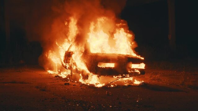 At night on street burning car in the city. Automobile engulfed in flames of fire. Explosion. Bomb. Car crash. Burning wheel. Emergency