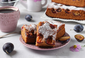 Honey pie with plums sprinkled with powdered sugar and cup of coffee on light gray table