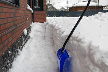 Blue snow shovel in the trench of snow. cleaning the path of country house after huge snowfall. a...