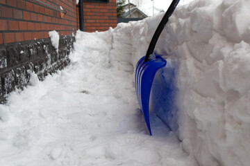 Blue snow shovel on the snow. cleaning the path of country house after a heavy snowfall. a cloudy...