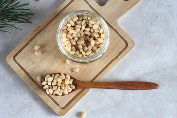 A jar of pine nuts lies on a wooden board on the table. There is a wooden spoon next to it. Top view