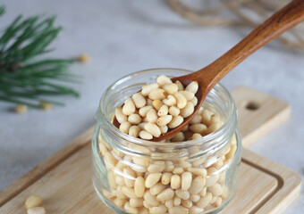 A jar of pine nuts lies on a wooden board on the table. Nuts are collected with a wooden spoon....