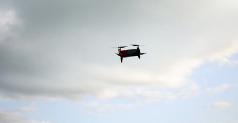 Hovering drone flying upward on a cloudy sky backdrop. copter flying .