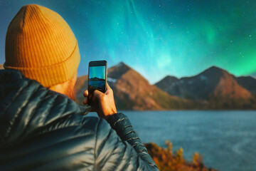 Man with smartphone taking photo of northern lights winter travel in Norway adventure vacations...