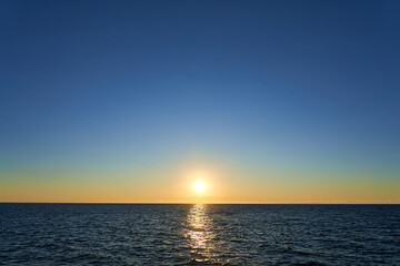 Naklejka na ściany i meble Sunset in the sea. The sun slowly goes behind the sea line