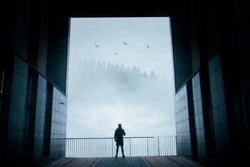 Fototapeta na wymiar A silhouette of a man, standing in between a huge futuristic gate, in front of a gorgeous foggy mountains landscape background. Idea concept of freedom, strategy, capability, and success.