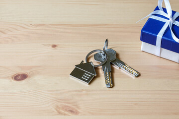 Keys with a keychain and a gift box with a bow on a wooden table. Places for text, Concept of buying a home, housewarming, real estate transactions.