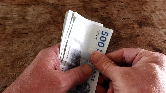A man counts 500 Danish Krone notes in his hands