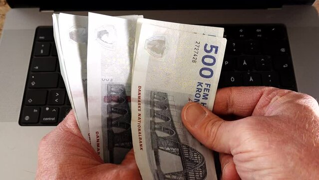 A man counts 500 Danish krone, Dansk krone, notes over a computer. 
