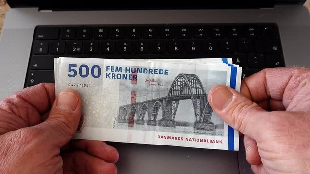 A man counts 500 Danish krone, Dansk krone, notes over a computer. 