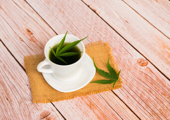 Hot Cannabis herbal tea and marijuana leaves on wooden table.