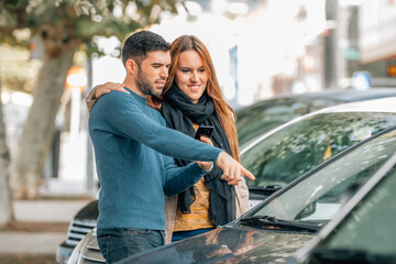 couple with mobile phone looking at cars to buy, buy car