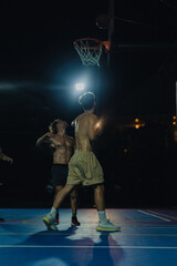 Fototapeta na wymiar Man friends play basketball in the open area. Night basketball game in the yard.