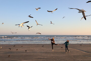 Two girls feeding flying seagulls on the beach - Powered by Adobe