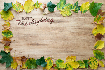 Naklejka na ściany i meble Happy Thanksgiving text with autumn leaves on light wood background