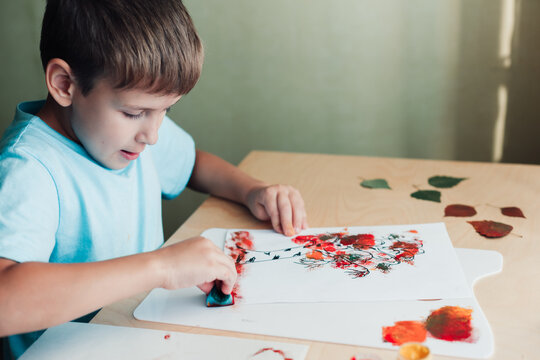 Cute child sitting at desk and making picture from colored dry birch leaves