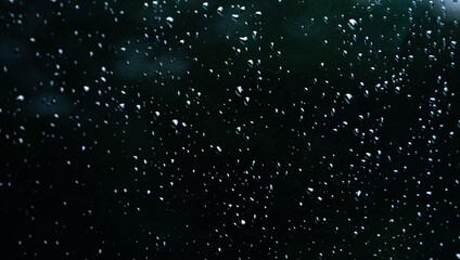 Round raindrops on a black surface. Drops on the glass. Rainy weather. Precipitation in the form of rain.