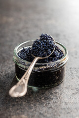 Naklejka na ściany i meble Black caviar in silver spoon on dark table.