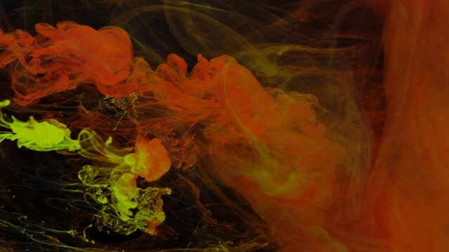 Stream of red and yellow paint dissolves in a transparent space on a black background.