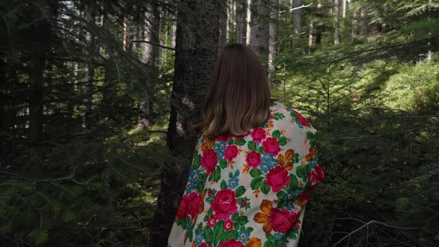 Back view of ukrainian woman with with traditional floral handkerchief walking in fir forest, Carpathian mountains nature. Ukraine, freedom, ethnic national costume