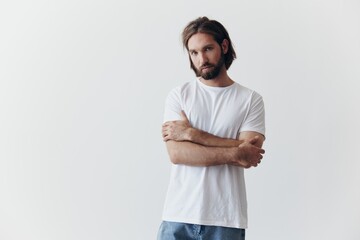 Portrait of a man with a black thick beard and long hair in a white T-shirt on a white isolated background emotion of sadness and longing