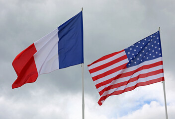 American and French flags with blue sky background waving together