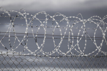 Barb wire roll on a fance barrier with dark clouds 