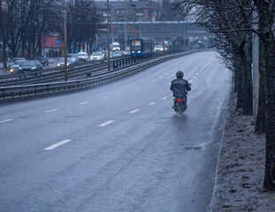 food delivery courier rides a motorcycle with a black thermal bag for delivering food in the rain along an empty road