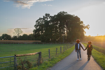 Fototapeta premium Pärchen mit Kürbissen auf dem Kopf geht im Sonnenuntergang spazieren 