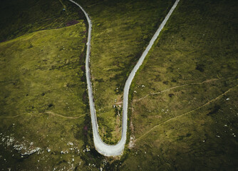Aerial photo of mountain curved roadunder the mountain peak in  Europe. Alpine road - beautiful scenic landscape with green meadows and rocks from above. Dark and moody photo of a way in mountains.