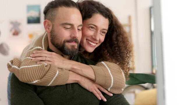 Woman embracing her husband while working from home in his workspace on a computer. Love, care and wife hugging her man from behind and kissing his cheek at remote job work desk in their modern house