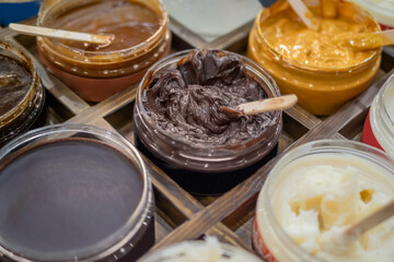 Set of jars with handmade body, face scrub with wooden stick on counter of cosmetic store. Treatment, care and wellness concept