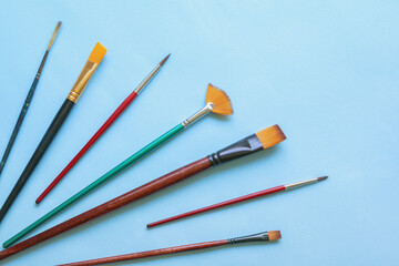 Various types of artistic paintbrushes on blue paper background. Copy space