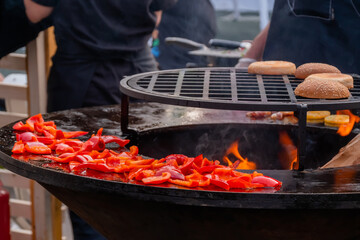 Naklejka premium Process of grilling healthy sliced red sweet bell pepper on brazier at summer outdoor food market - close up. Professional cooking, cookery, gastronomy and street food concept