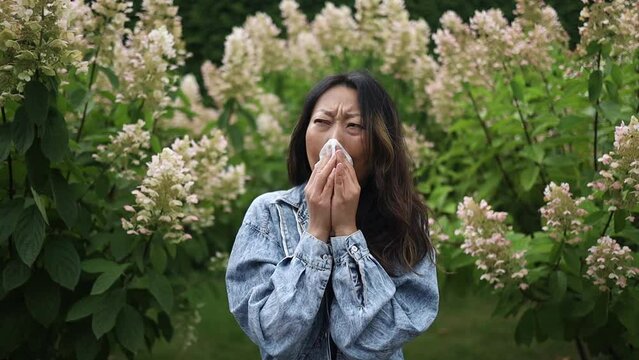 Sneezing young asian girl with nose wiper among flowering trees in the park