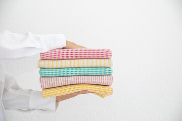 woman holding a collection of towels in a basket made of natural materials on a white background. Natural, soft, airy and stylish kitchen textiles.