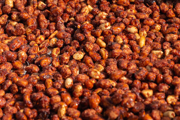 Heap of roasted caramelized sugared peanuts with warm and contrast sunlight illumination at summer outdoor food market - close up. Cookery, dessert, gastronomy and street food concept