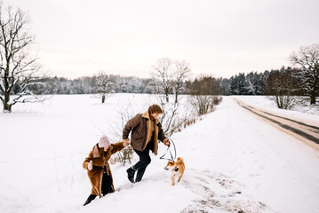 Cute young couple having fun in the winter park with their dog on bright day.Man and woman are relaxing