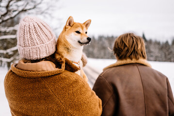 Cute young couple having fun in the winter park with their dog on bright day.Man and woman are relaxing