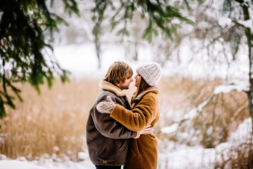 Cute young couple in love having fun in the winter park on bright day. Woman and man relaxing outdoors