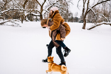 Cute young couple having fun in the winter park with their dog on bright day.Man and woman are relaxing