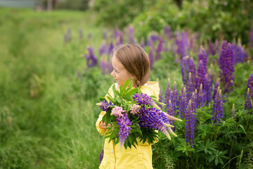 Naklejka premium portrait of a cute little happy eight-year-old girl in a yellow jacket with blooming lupine flowers in a field of purple flowers. nature in the open air. The concept child in nature. Summer holidays
